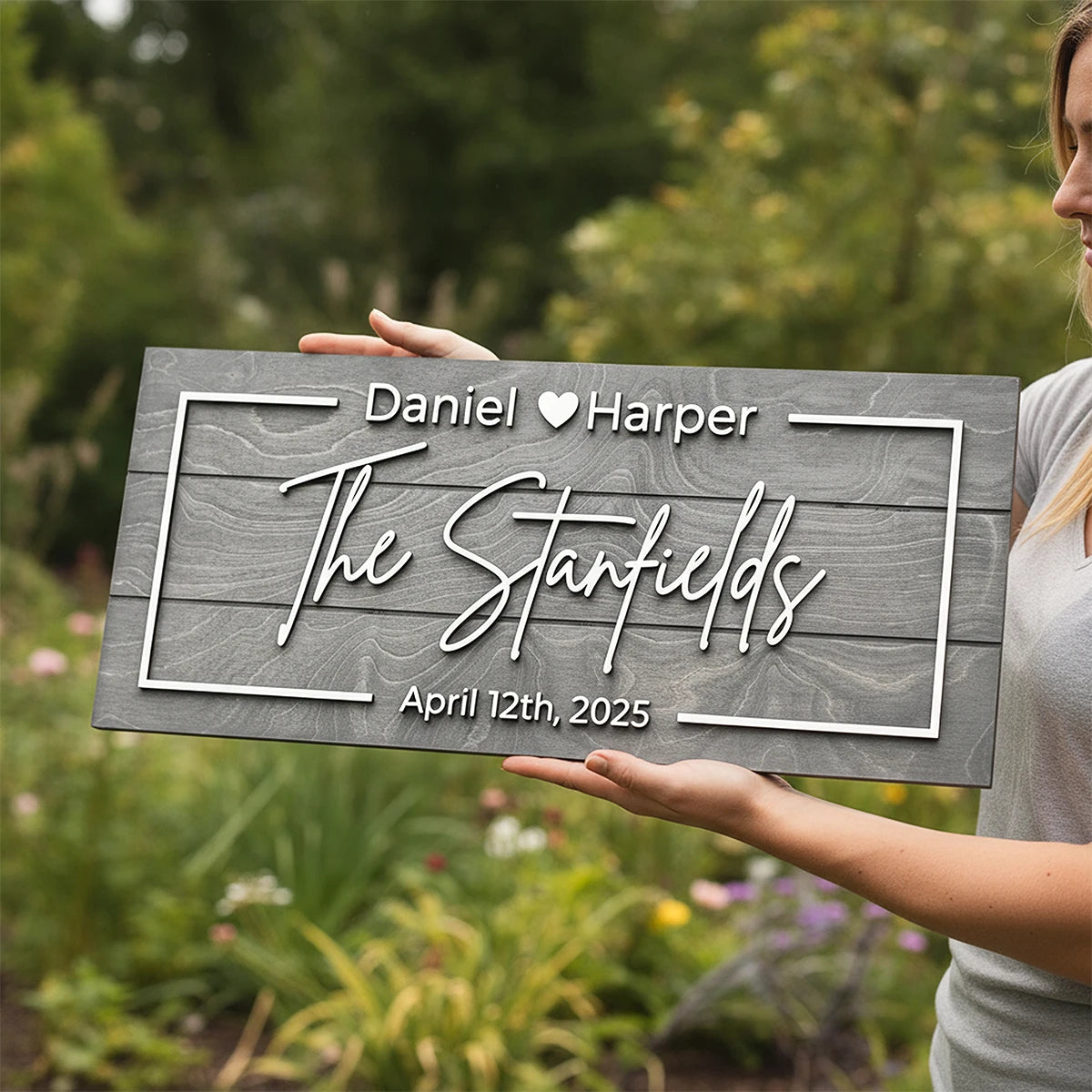 Person holding a personalized wooden sign with 'The Stanfields' and date in a garden setting
