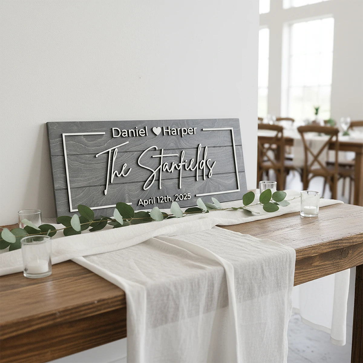 Personalized wooden sign on a table with a white runner and greenery