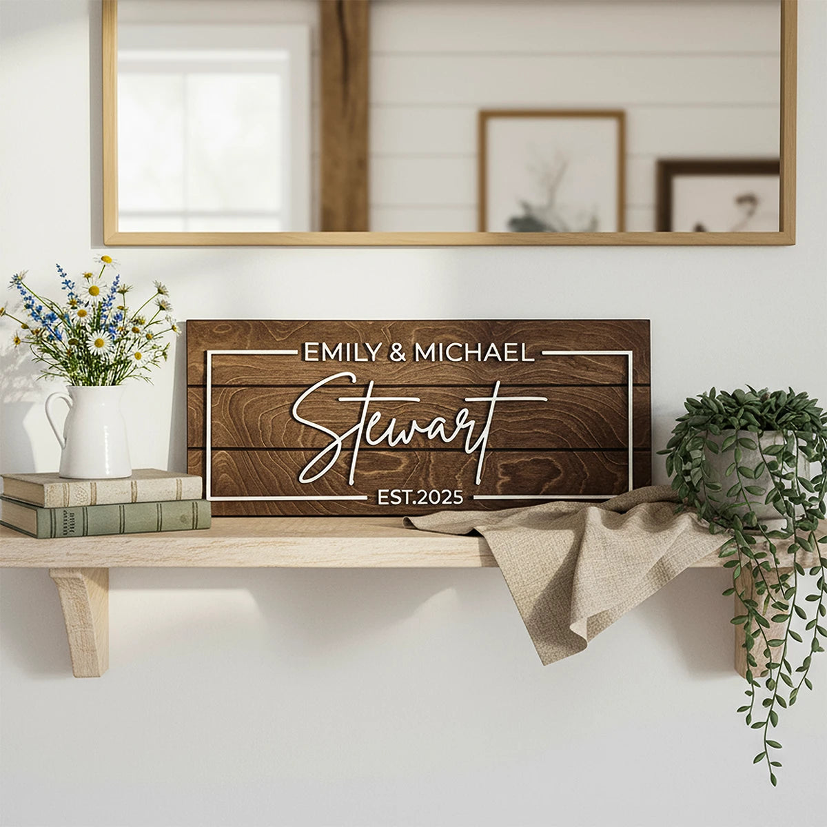 Wooden sign with 'Emily & Michael Stewart EST.2025' on a shelf with decor items.