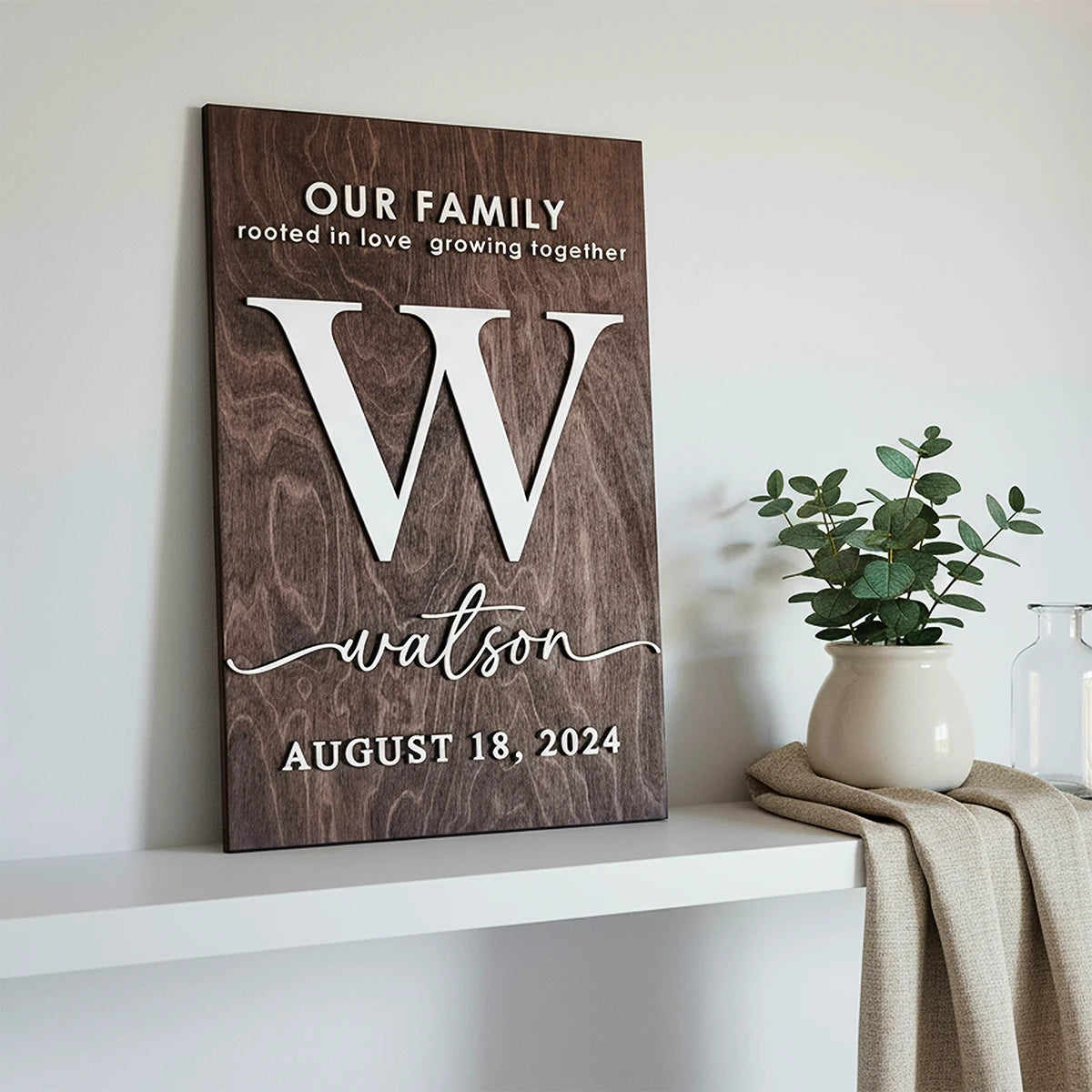 Wooden wall art with family name and date on a shelf with a plant and blanket.
